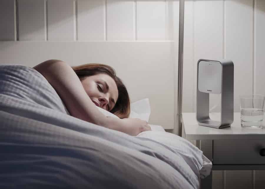 A woman sleeping peacefully next to nightstand with a sleep apnea machine with humidifier next to her on her nightstand after a sleep study administered by Whitney Sleep in Plymouth, Minnesota