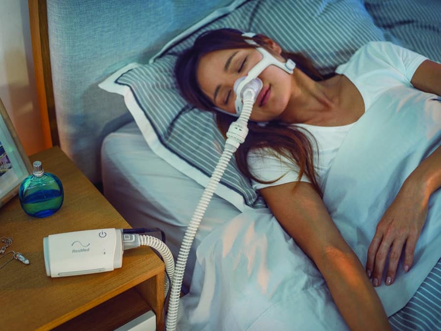 A woman lies asleep wearing a sleep apnea nasal mask connected to a ResMed sleep apnea machine for a sleep study with Whitney Sleep in Burnsville, Minnesota