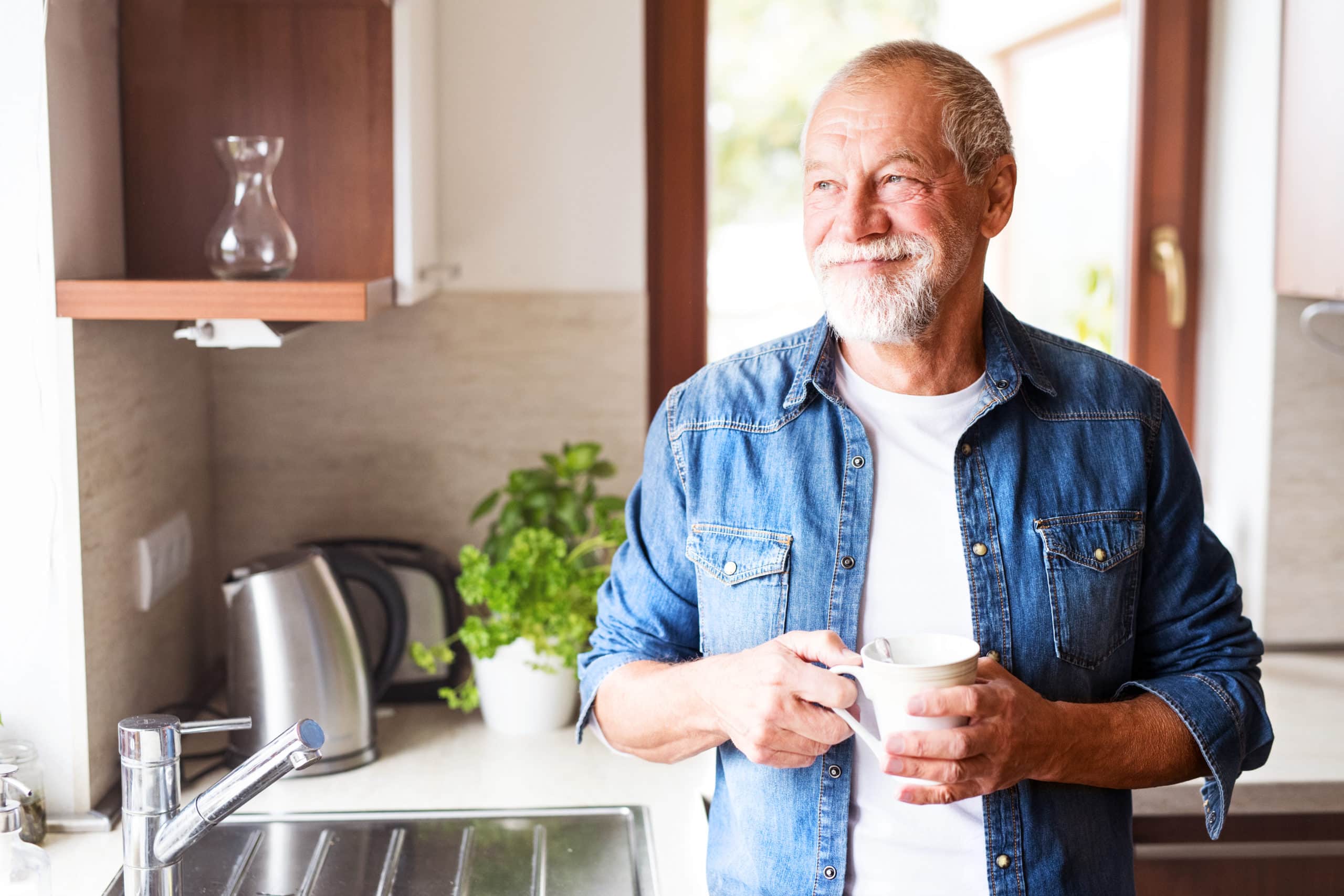 A happy elderly man holding a cup of coffee in a kitchen.