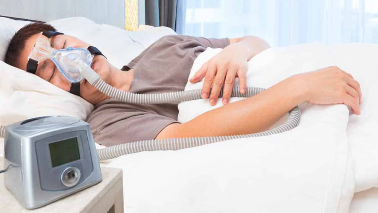 A man sleeps comfortably at a hotel while traveling with a CPAP machine.
