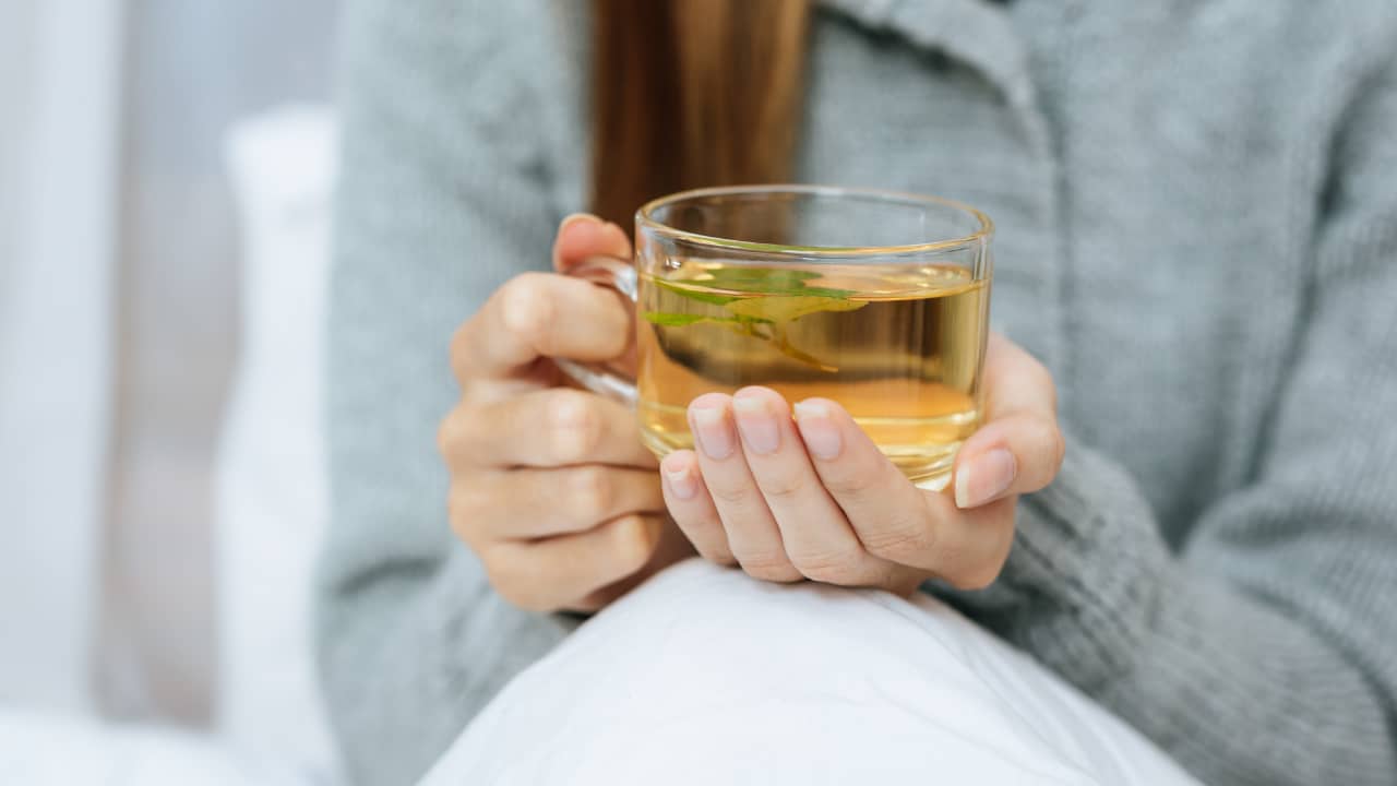 A woman holds a glass of chamomile tea, one of the drinks at bedtime recommended by Whitney Sleep Specialists to improve sleep.